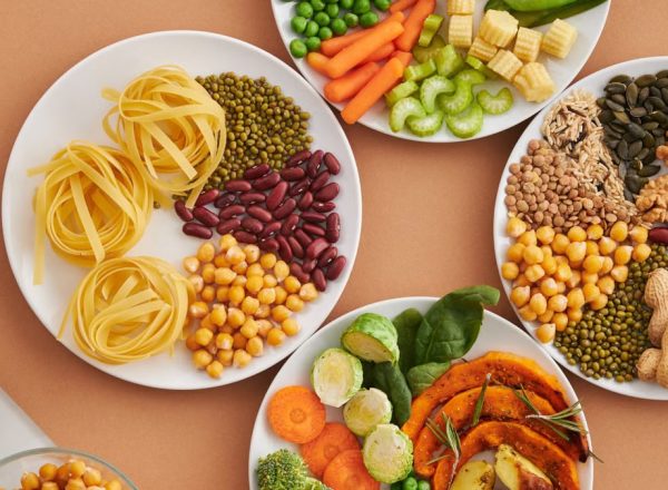 A vibrant mix of legumes, vegetables, nuts, and pasta arranged on white plates showcasing a balanced, healthy diet.